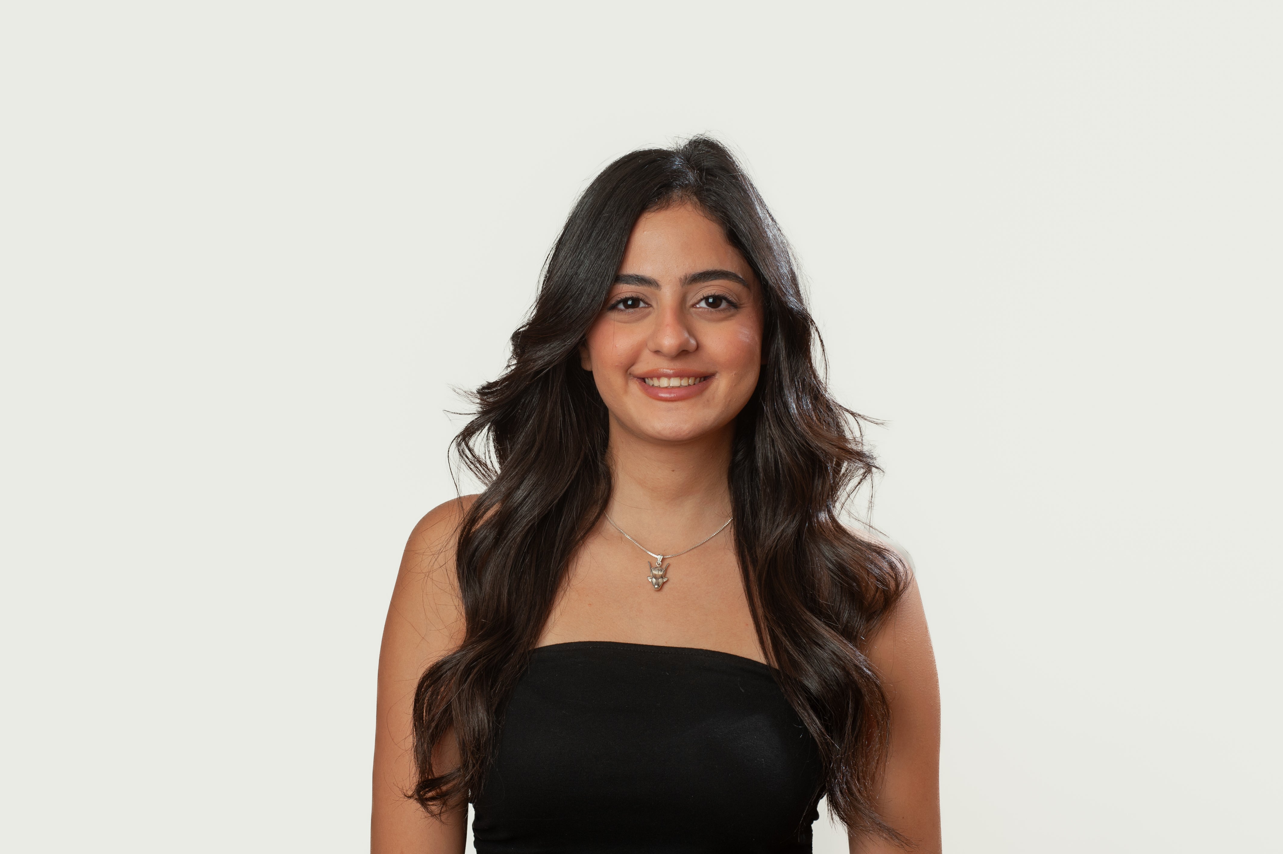 Woman with long dark hair wearing a black top against a plain background