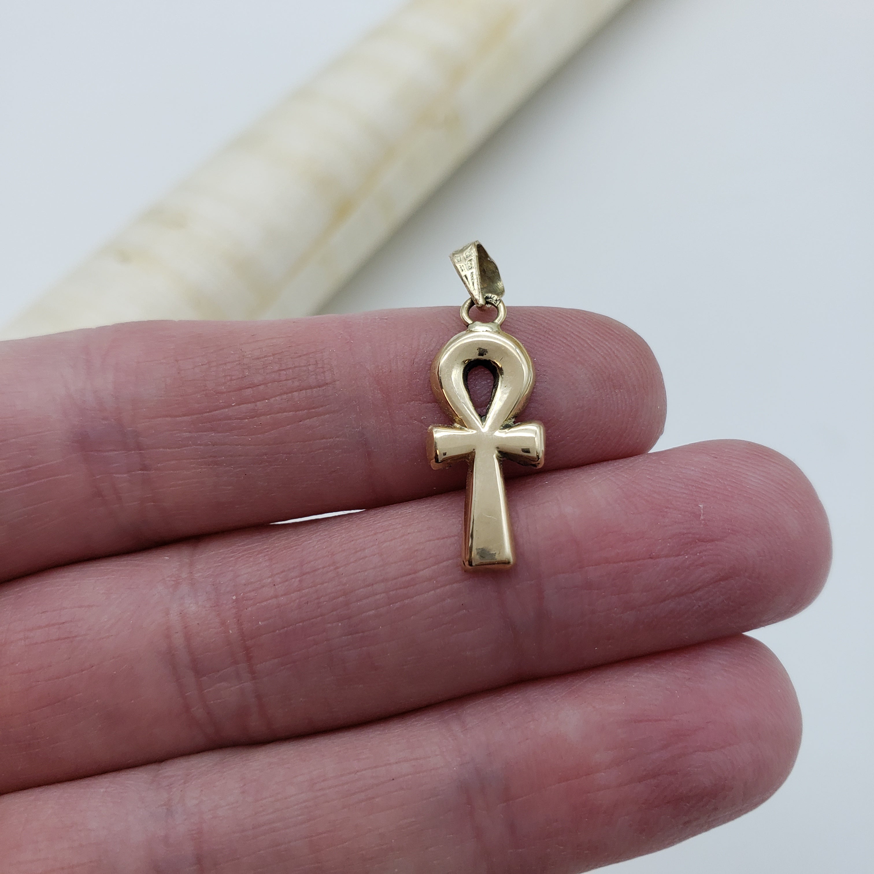 Gold ankh pendant on a finger with a white background