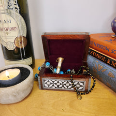 Bracelet with blue beads on a wooden box next to a bottle of wine and a lit candle.