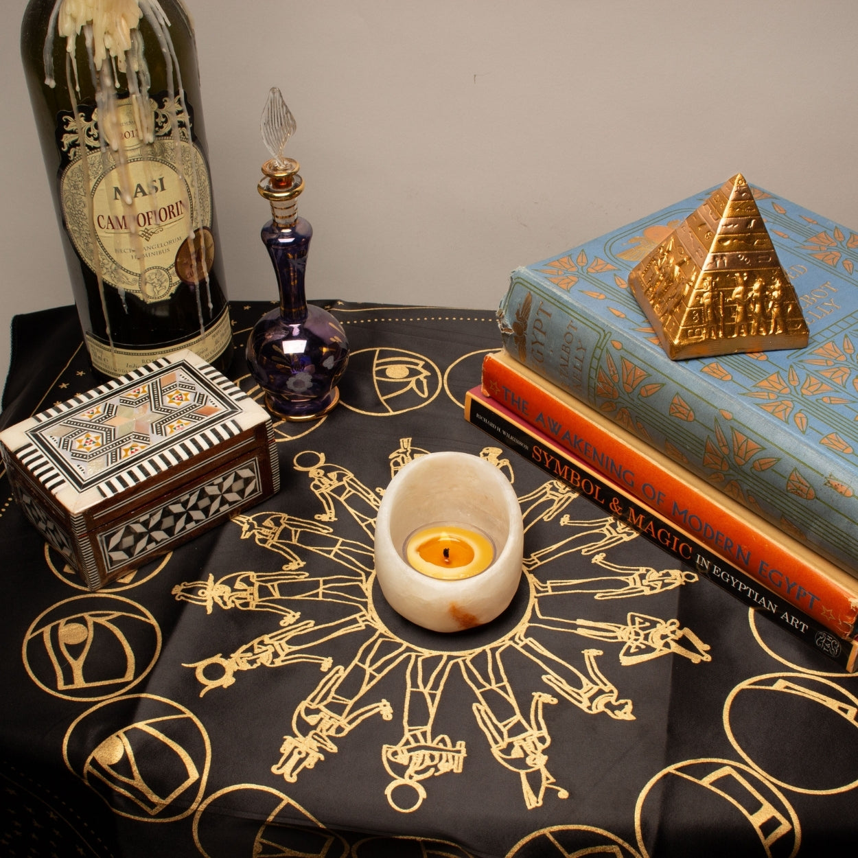 Decorative setup with books, a bottle, and a candle on a table with mystical symbols.