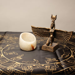 Bronze statue of a winged creature and white stone candleholder on an astrological map.