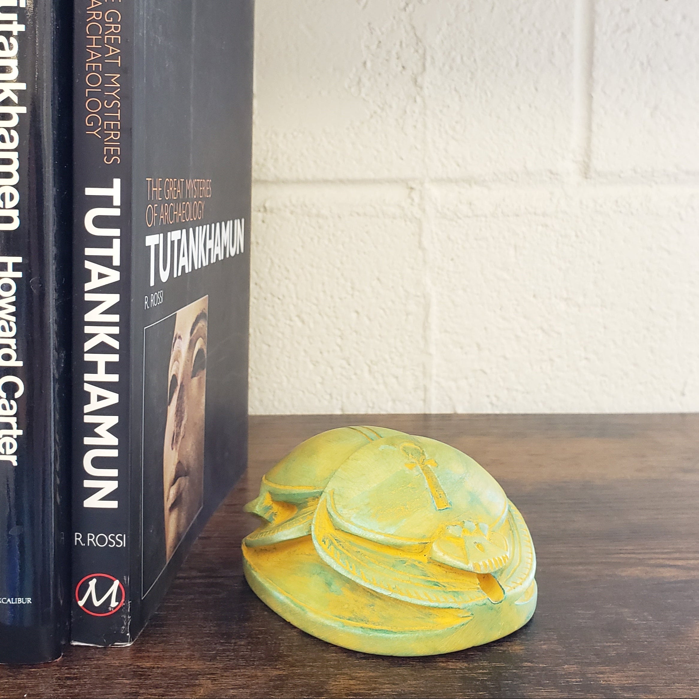Two books titled 'Tutankhamun' and 'The Tomb of Tutankhamen' by Howard Carter on a wooden surface with a decorative wall piece.