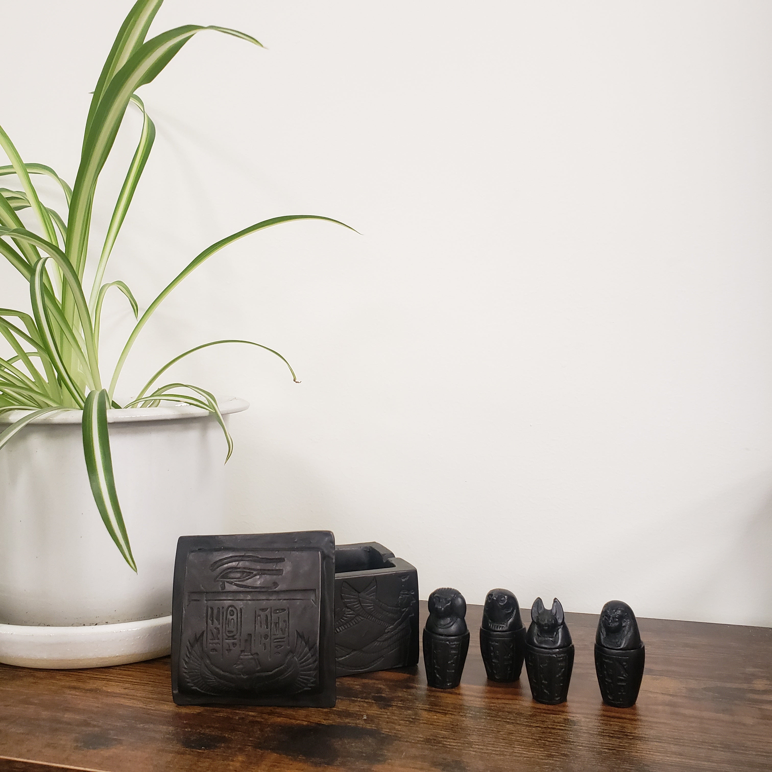 Set of black statues on a wooden block with a plant in the foreground