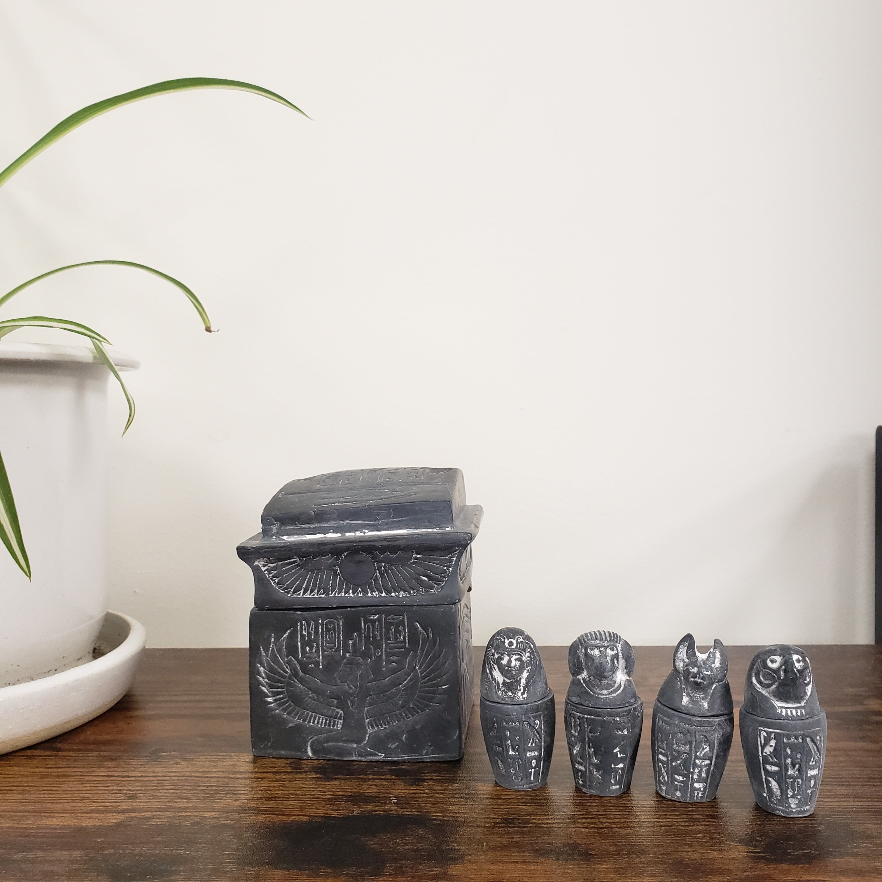 Decorative stone statues on a wooden shelf with a plant in the foreground