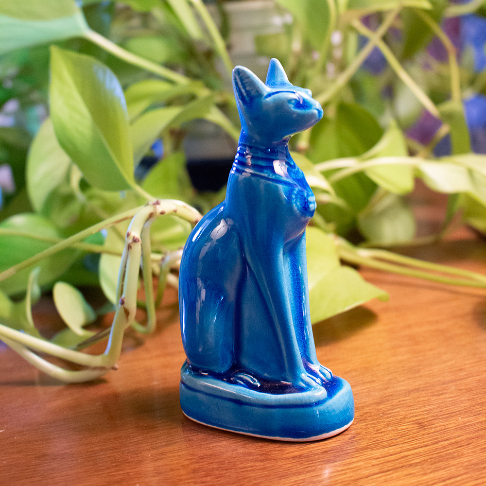 Blue cat figurine on a wooden surface with green leaves in the background