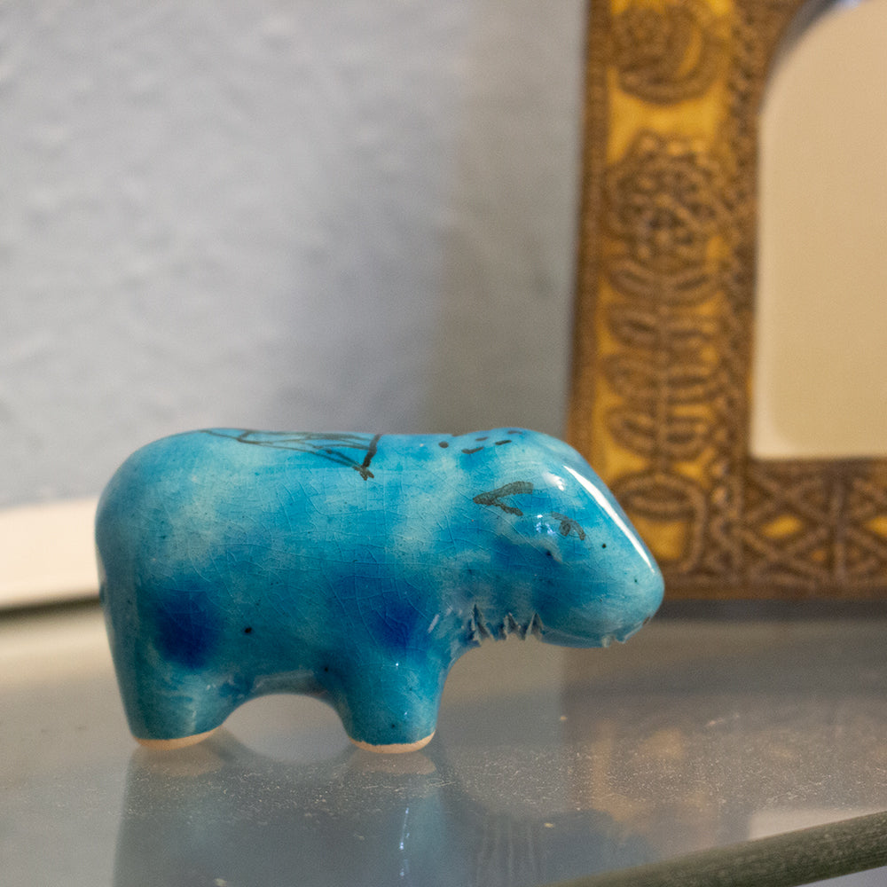 Blue ceramic hippo figurine on a reflective surface with a blurred background