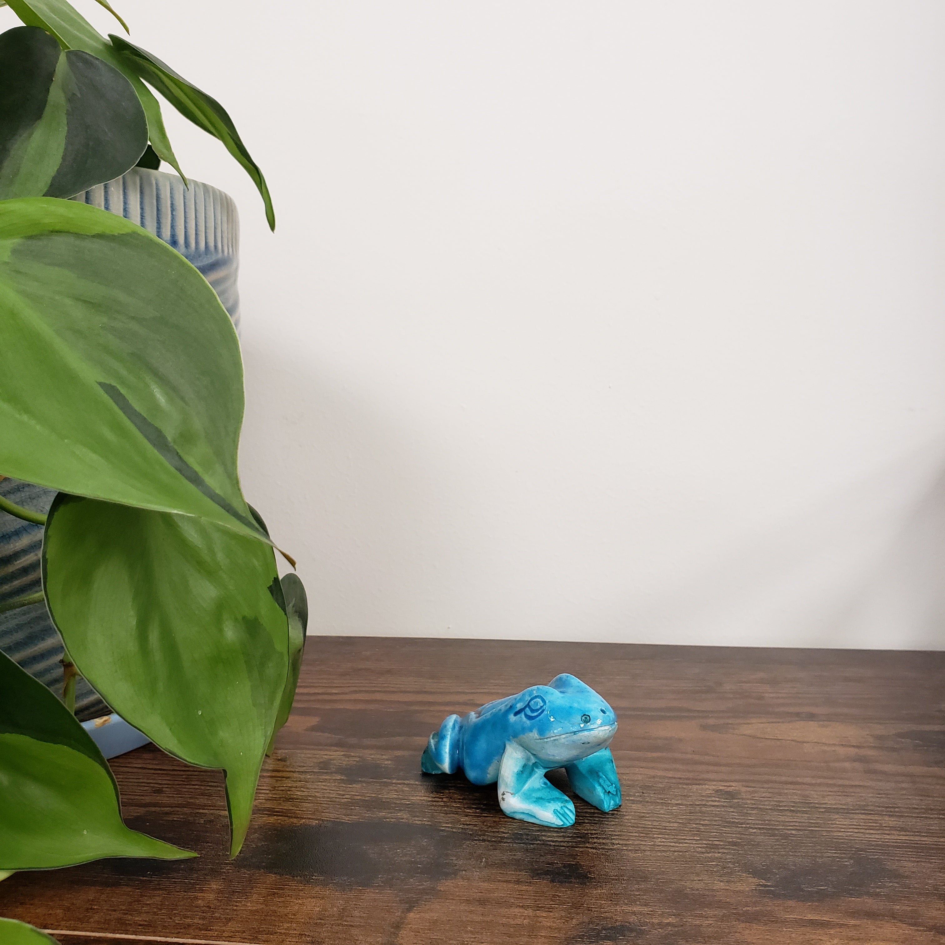 Blue ceramic frog figurine on a wooden surface with green leaves in the foreground