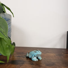 Decorative blue frog-shaped statue on a wooden door with plants and a striped cushion in the background.