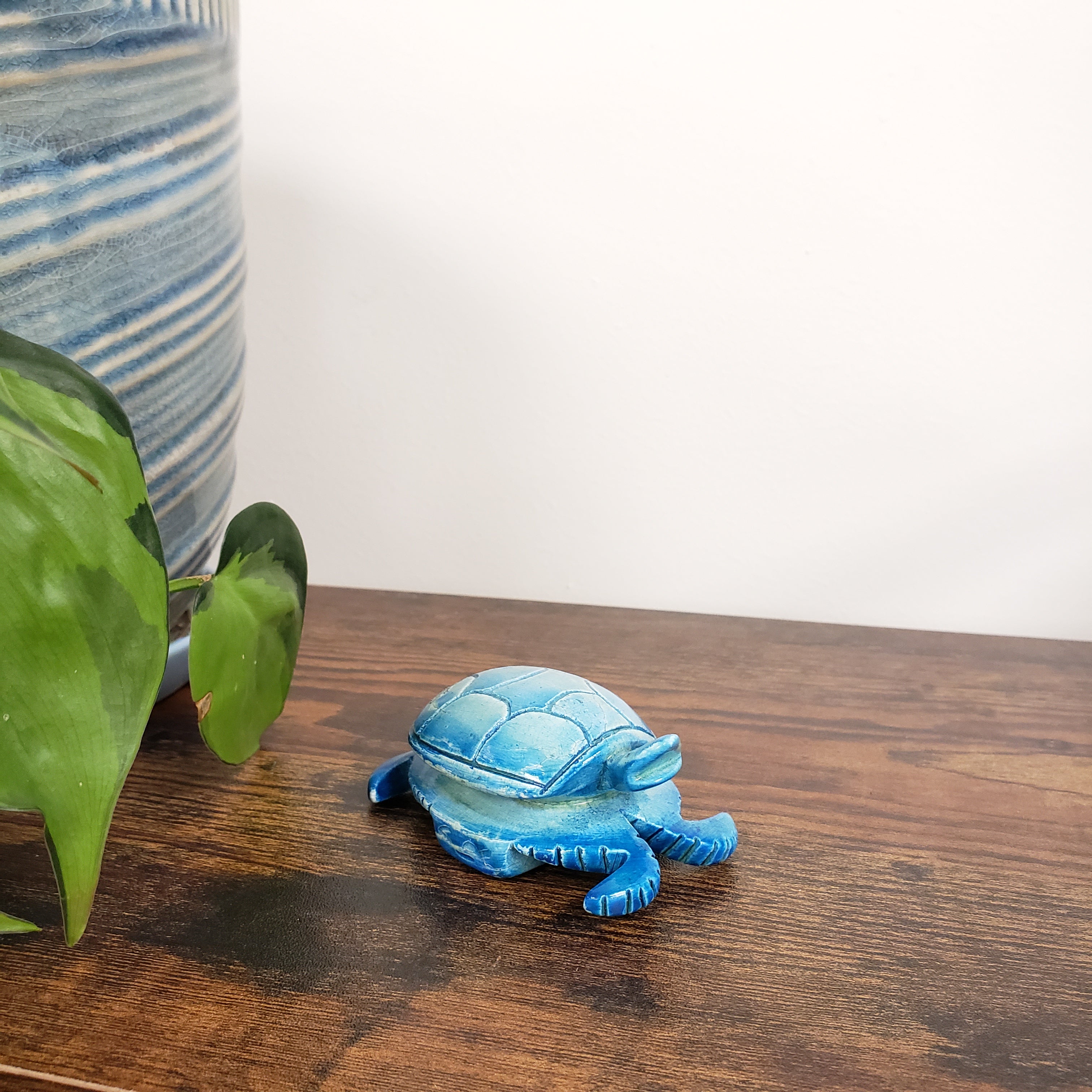 Blue turtle-shaped decorative item on a wooden surface with a plant in the foreground.