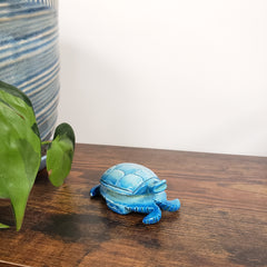Blue turtle-shaped decorative item on a wooden surface with a plant in the foreground.