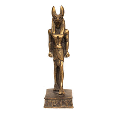 A small bronze-finished statue of an ancient Egyptian deity with a canine head, standing on a rectangular base with hieroglyphic details, isolated on a white background.