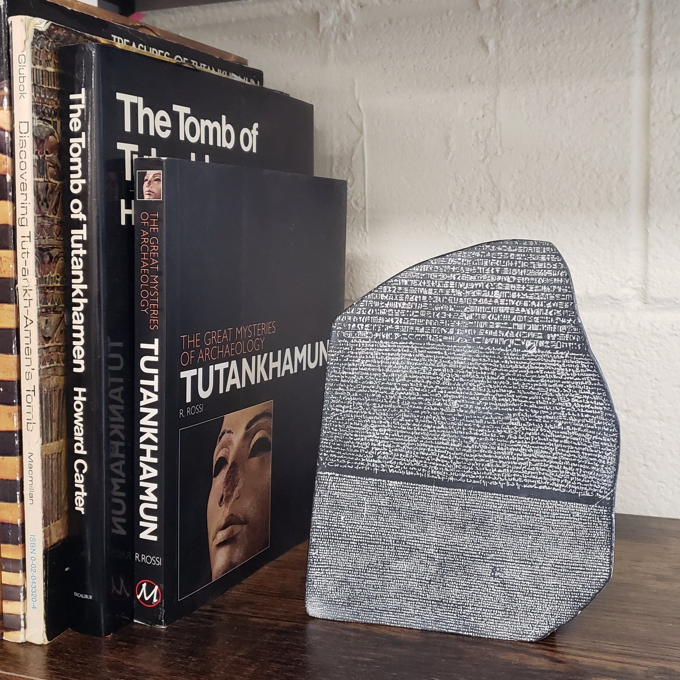 Stack of books on Tutankhamun with a stone tablet on top, against a wooden and stone wall background.