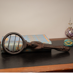 A decorative dark brown carved Egyptian sistrum rattle with a circular loop and ornate handle, displayed on a black tabletop with a blue patterned book and a small purple glass object in the background.