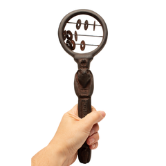 A hand holding a dark brown Egyptian sistrum rattle with circular wire details, shown against a plain white background.