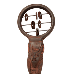 A rustic metal tool with a circular top containing several small round metal discs on a wire frame, attached to a carved handle with a face motif, shown on a plain white background.