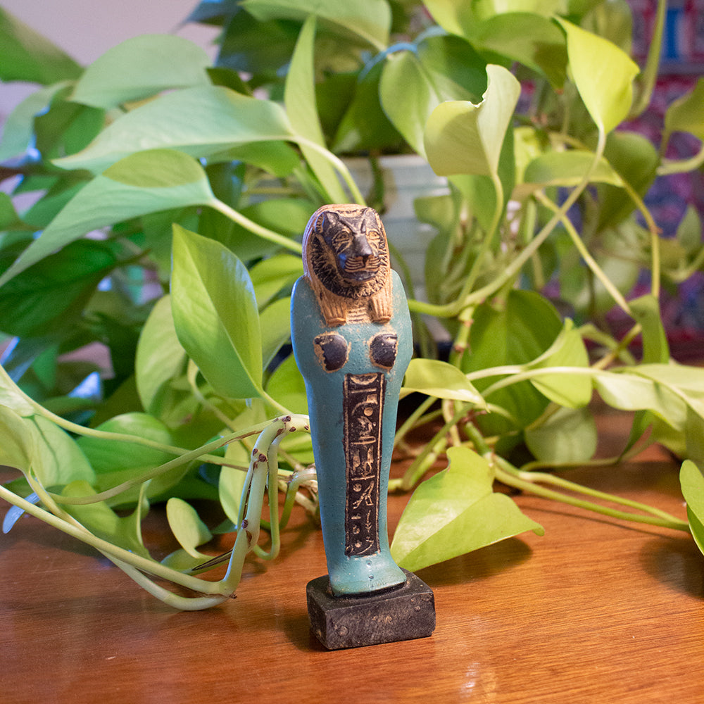 Decorative figurine with a lion's head on a wooden surface with plants in the background