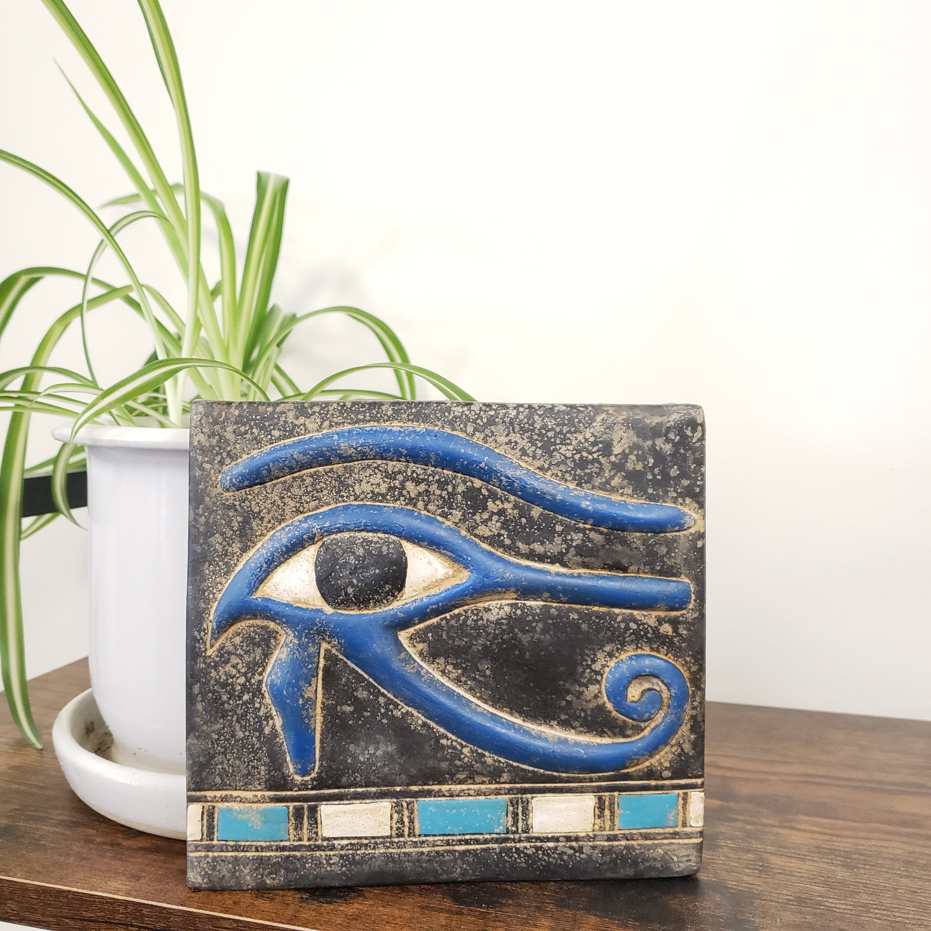 Decorative wall art with blue eye design on a wooden surface with a plant in the background