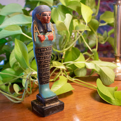 Decorative Egyptian-style figurine on a wooden surface with green leaves in the background