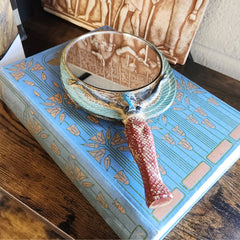 Decorative hand mirror with a red handle on a blue book with gold patterns