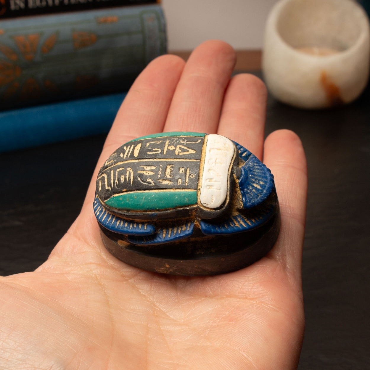 Hand holding a decorative object with hieroglyphics against a blurred background