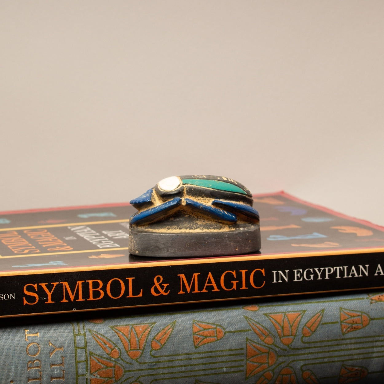 Decorative object on top of a book titled 'Symbol & Magic in Egyptian Art' with a plain background.
