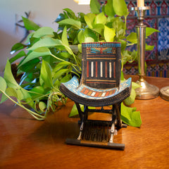 Decorative chair model on a wooden surface with plants and a candle in the background