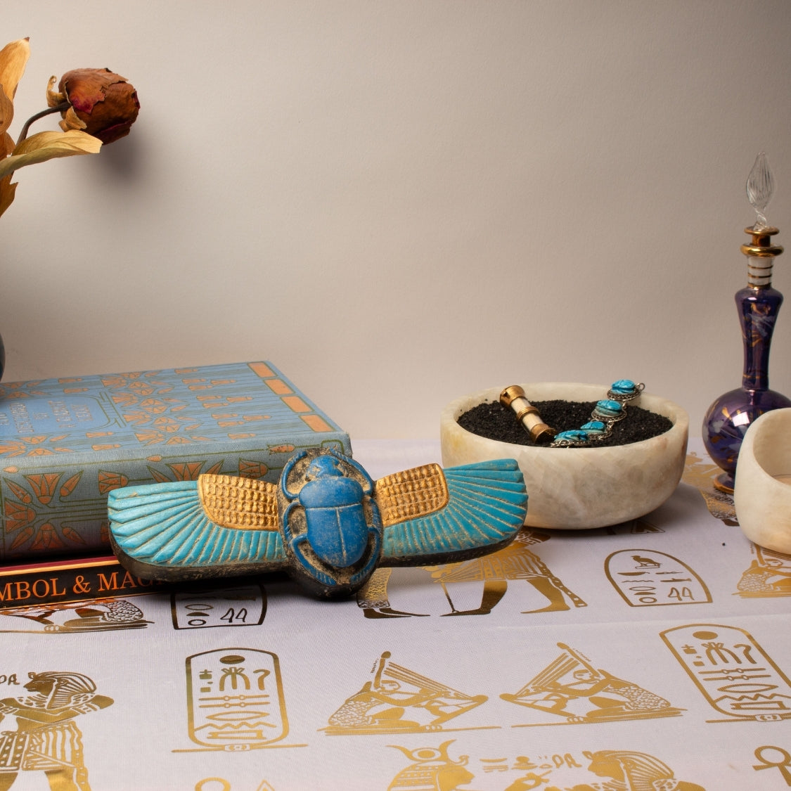 Decorative items including a blue scarab, book, and bowl on a surface with hieroglyphics.