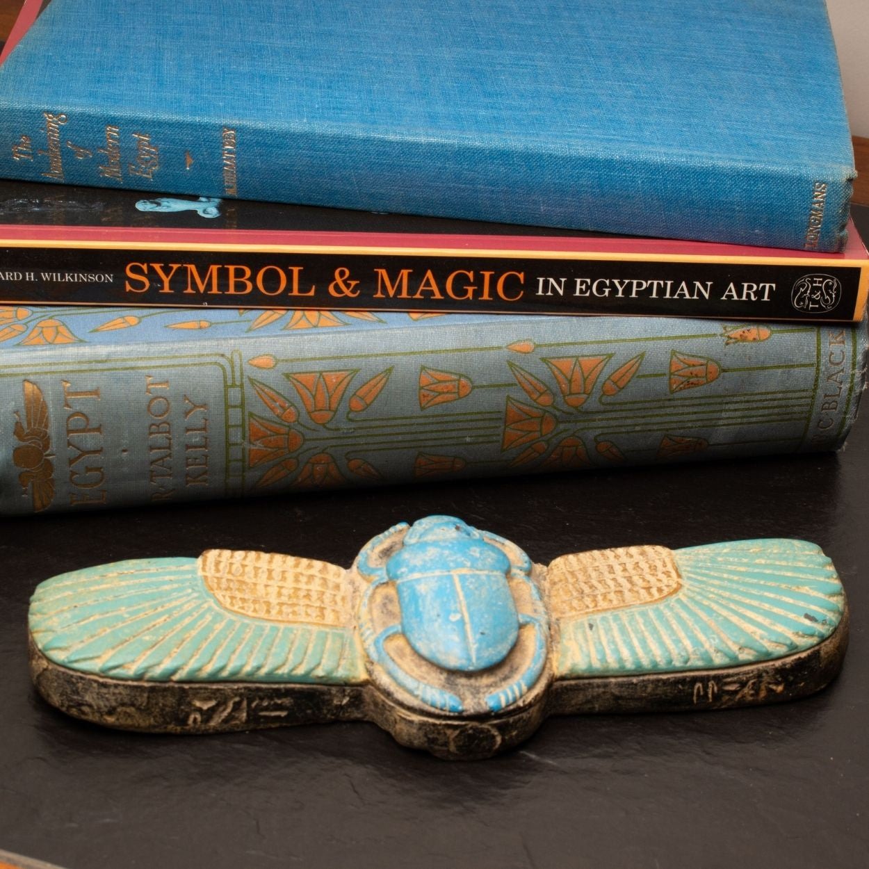 Decorative scarab with Egyptian design on a dark surface with books in the background