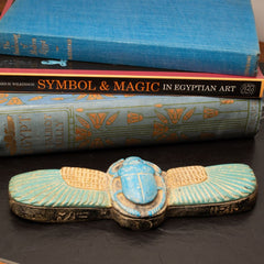 Decorative scarab with Egyptian design on a dark surface with books in the background