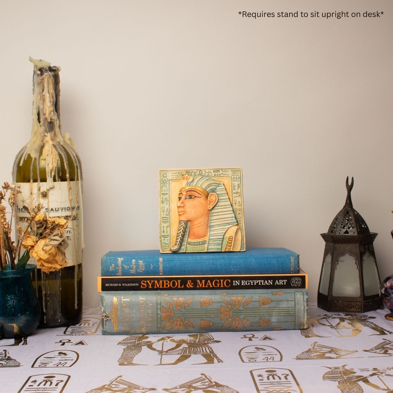 Decorative setup with books, a statue, and a bottle on a table with an Egyptian-themed tablecloth.