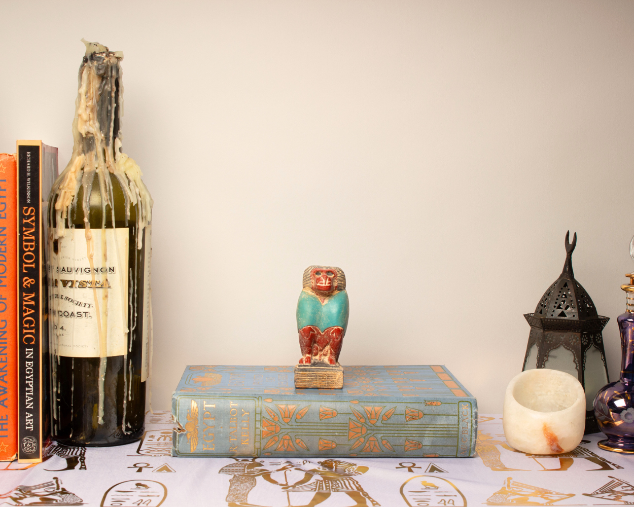 Decorative setup with books, a bottle, a candle, and a figurine on a table.
