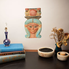 Decorative wall hanging of an Egyptian-style face on a wall above books and decorative items.