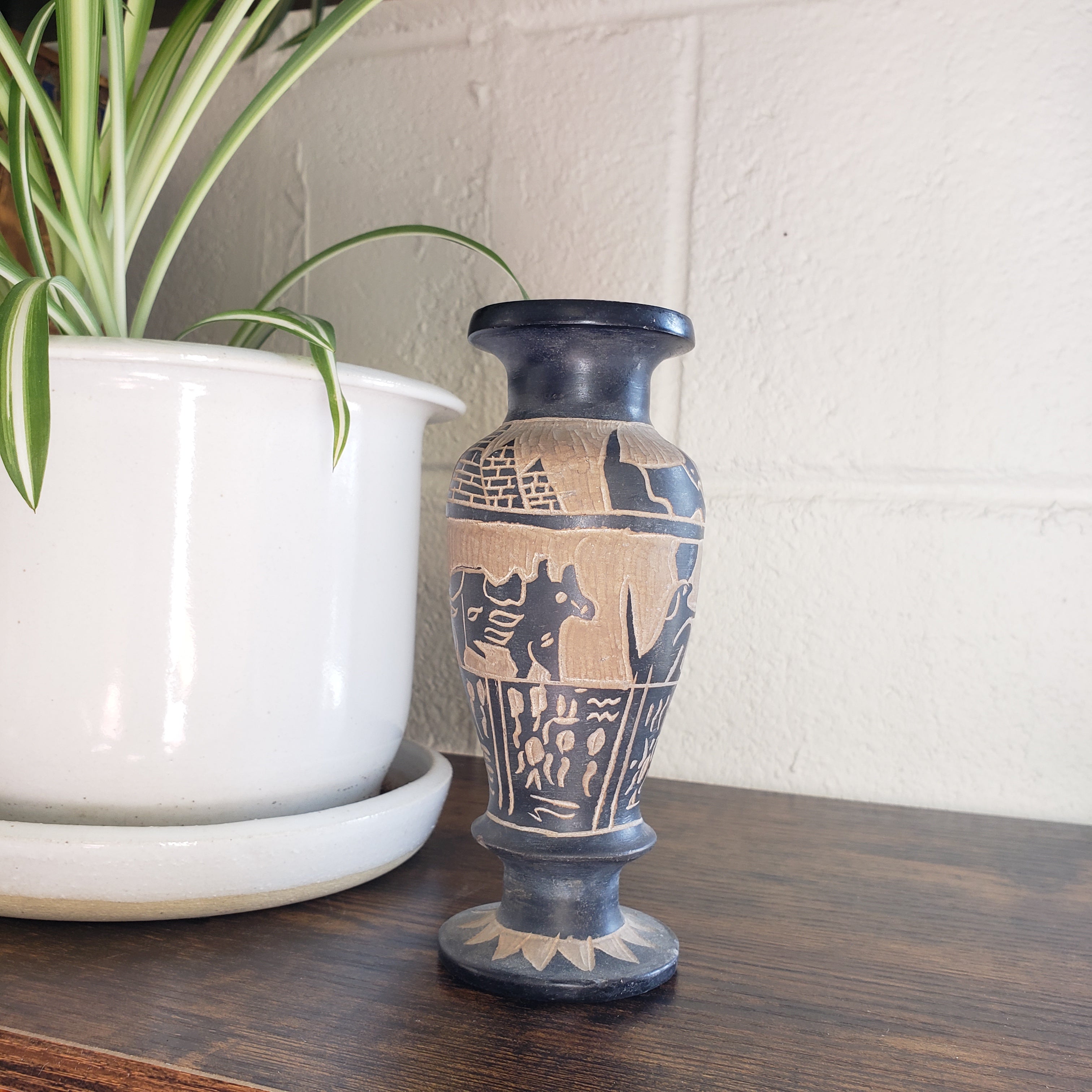 Decorative vase with intricate patterns on a white surface next to a plant