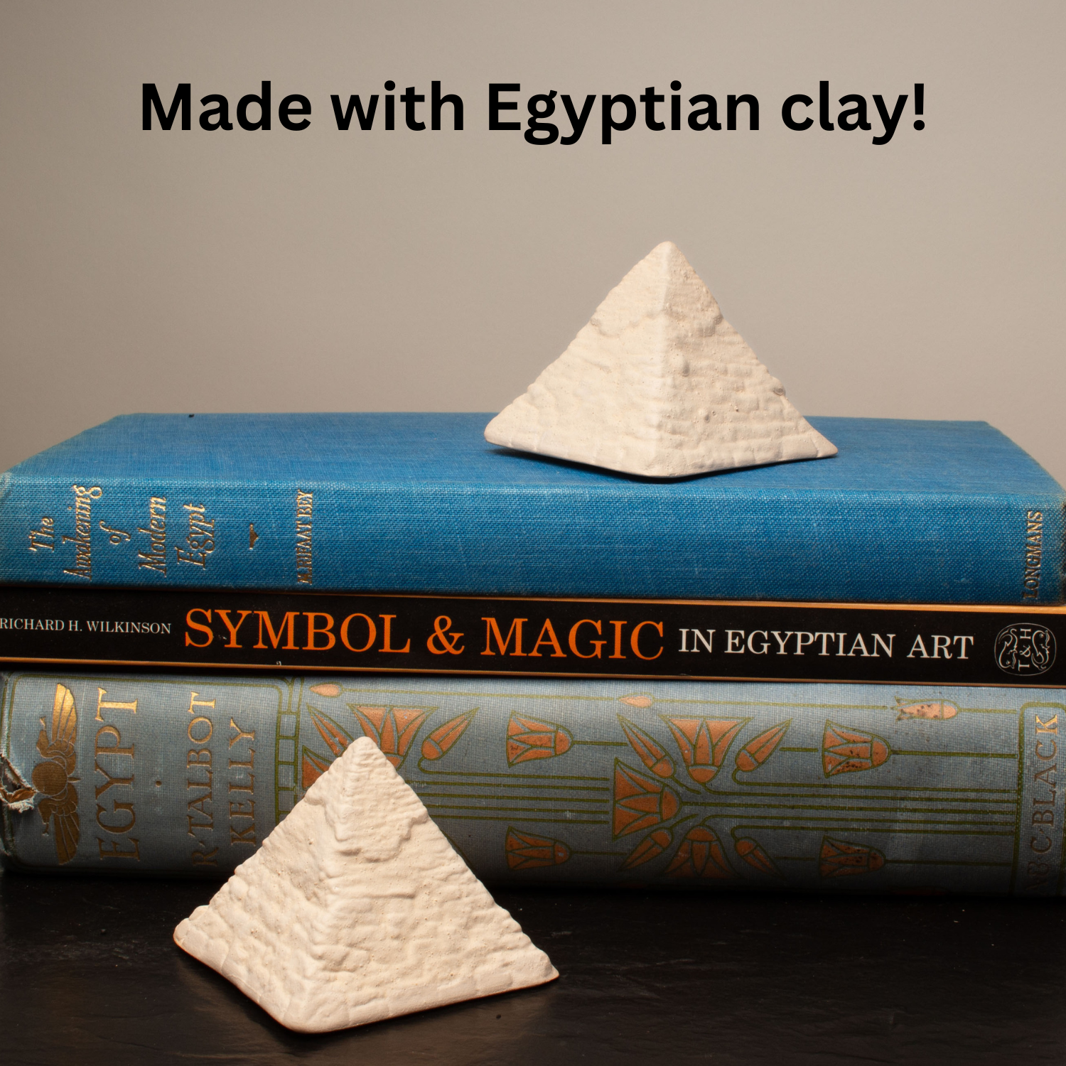 Two small white pyramid-shaped clay objects displayed on top of and in front of two decorative books, with the text 'Made with Egyptian clay!' above the scene.