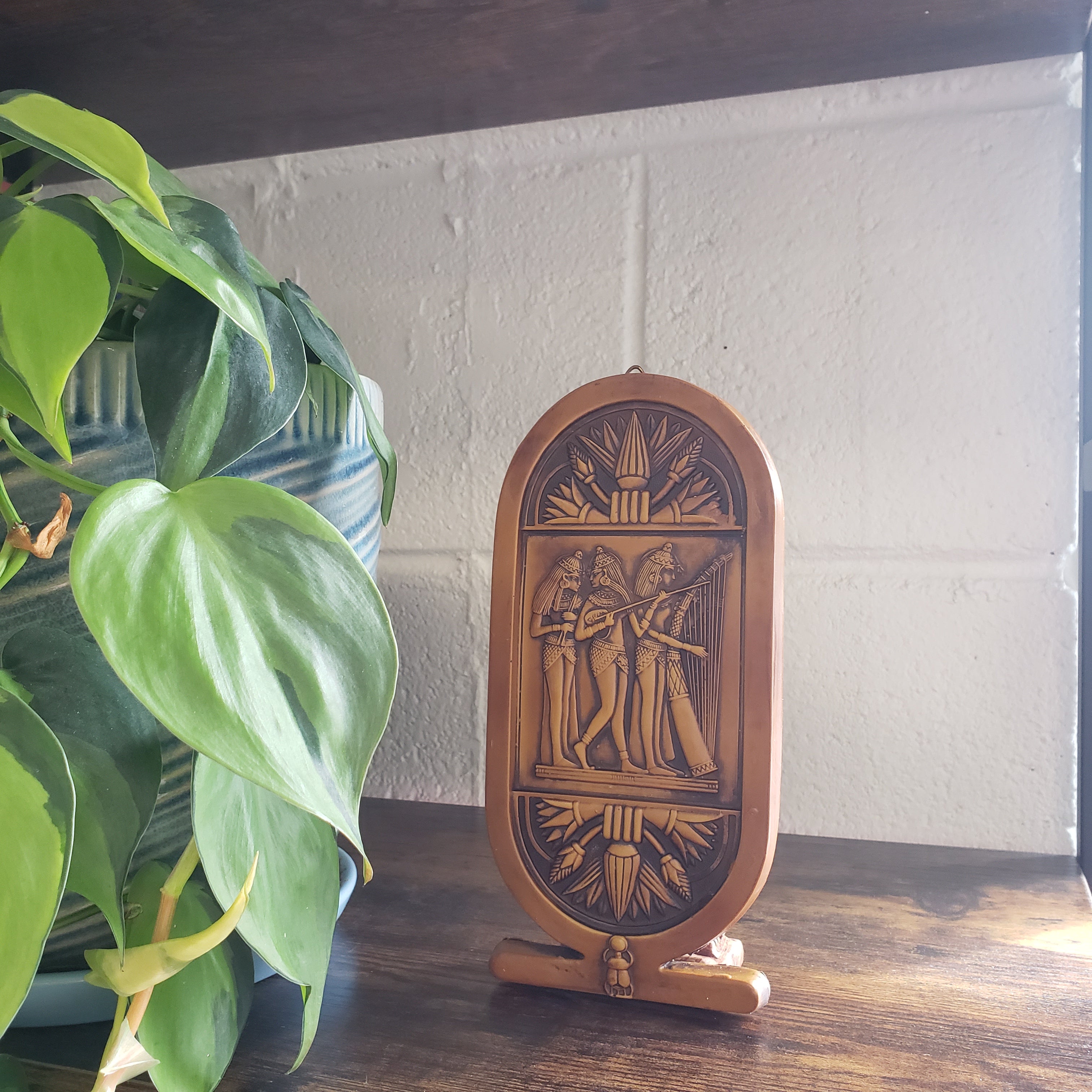 Decorative plaque with intricate carvings on a wall next to a potted plant.