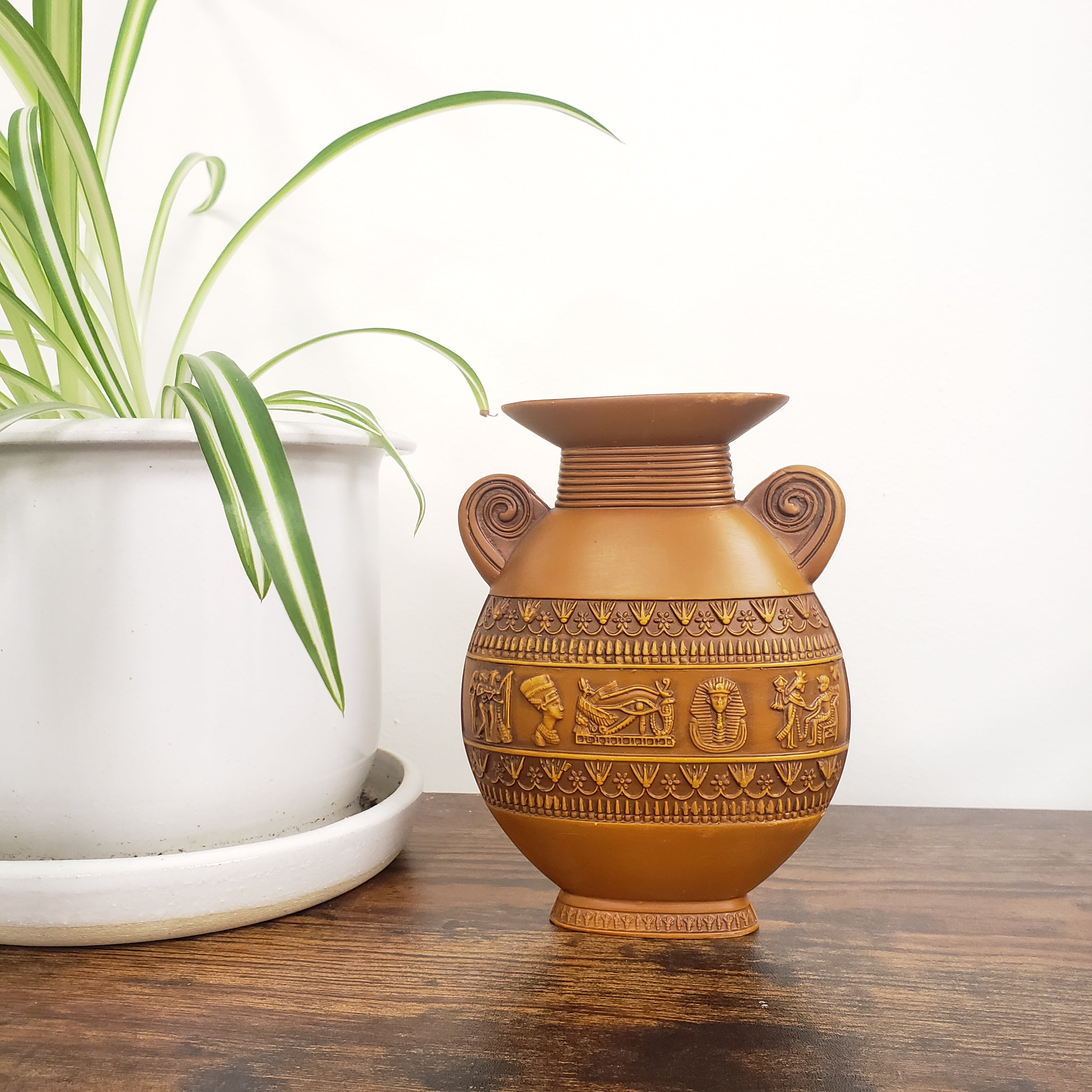 Decorative brown vase with intricate patterns on a white surface next to a plant