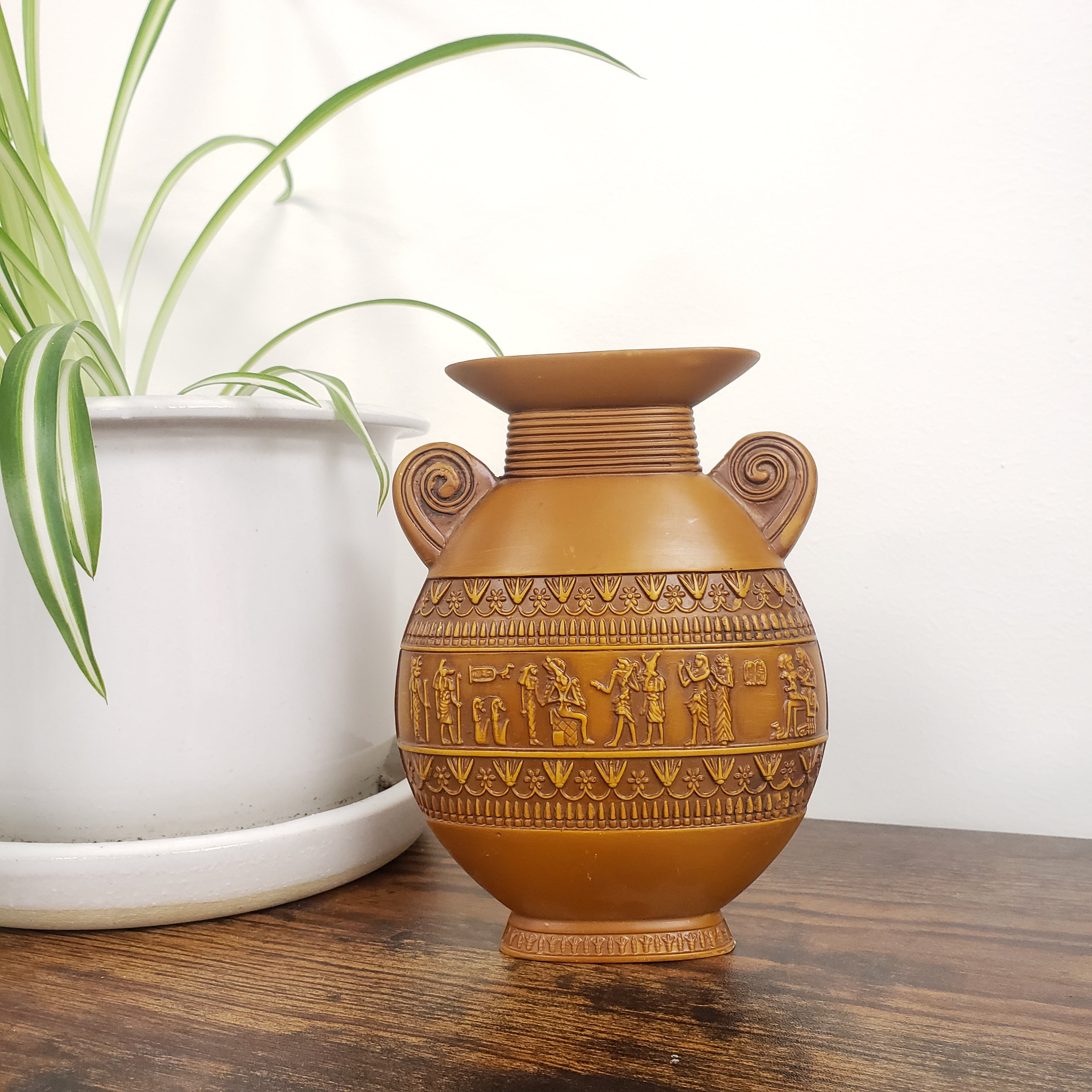 Decorative brown vase with intricate patterns on a white surface with a plant in the background