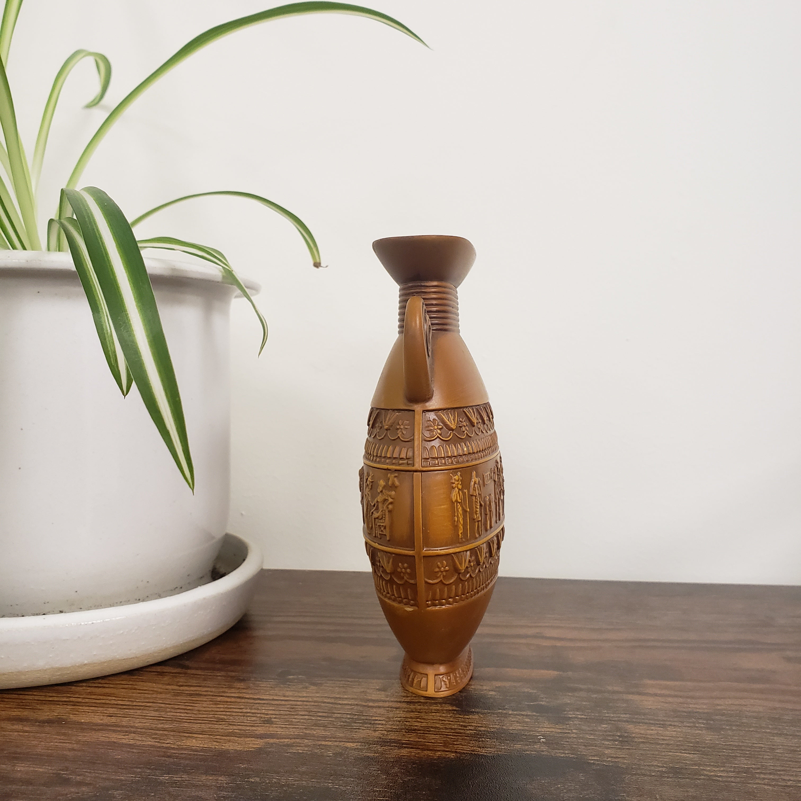 Decorative brown vase with intricate patterns on a wooden surface next to a plant.