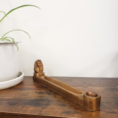 Bronze incense holder on a wooden surface with a white wall and plant in the background
