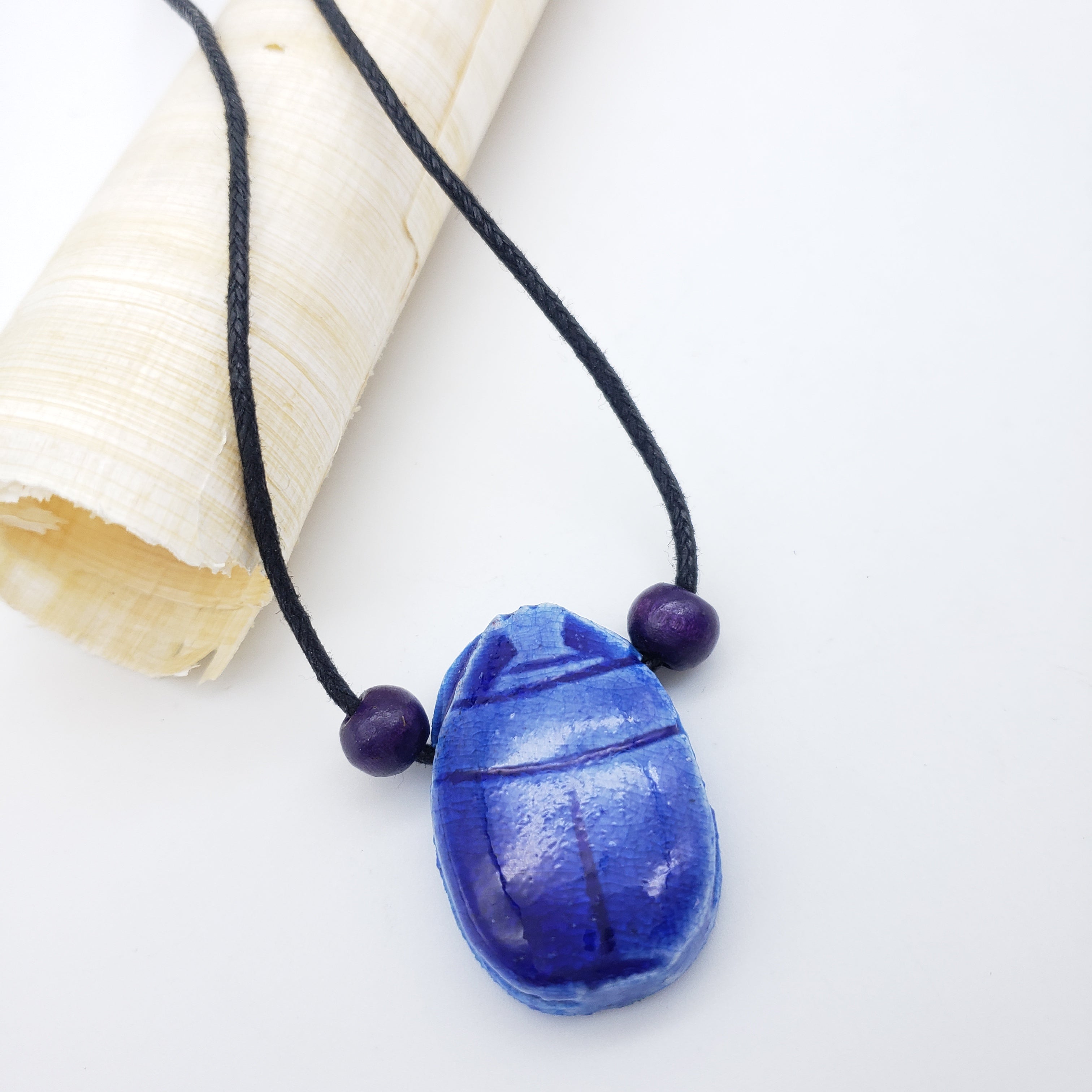 Blue scarab necklace with purple beads on a white background