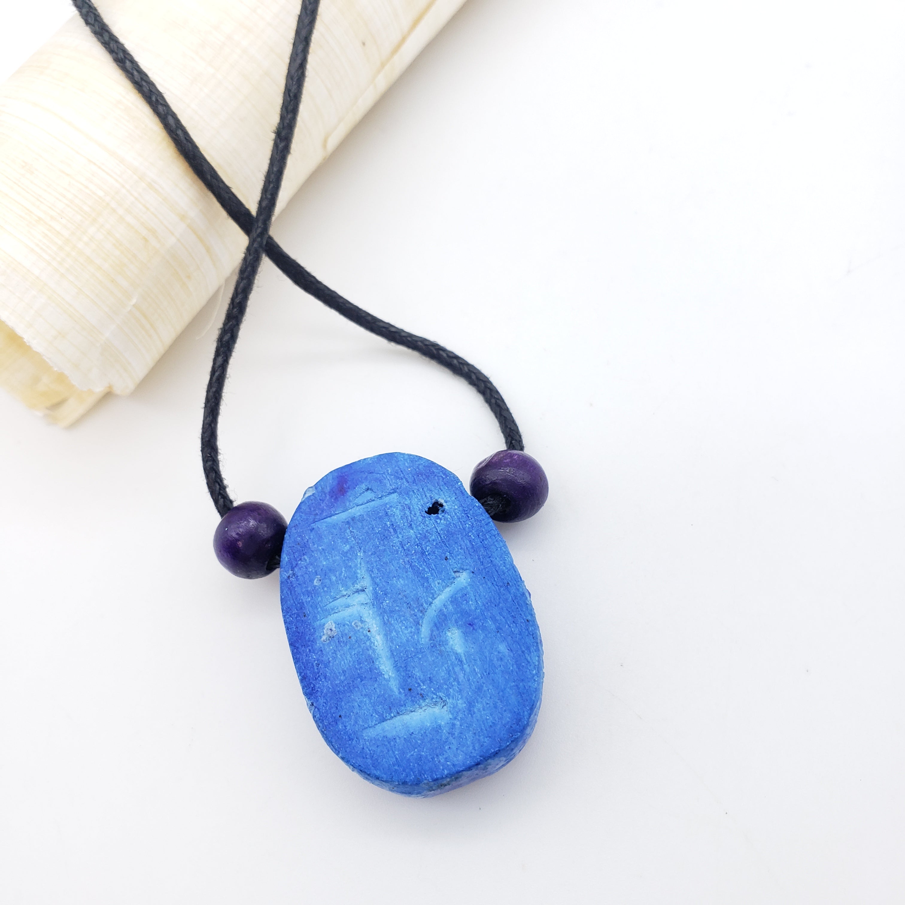 Blue stone pendant with black cord on a white background