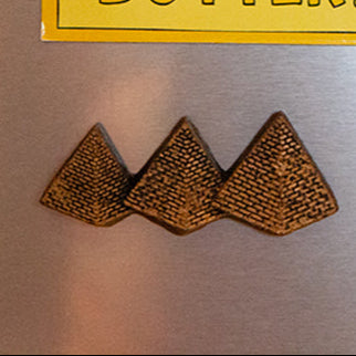 Three brown triangular shapes on a metallic surface with a yellow border.