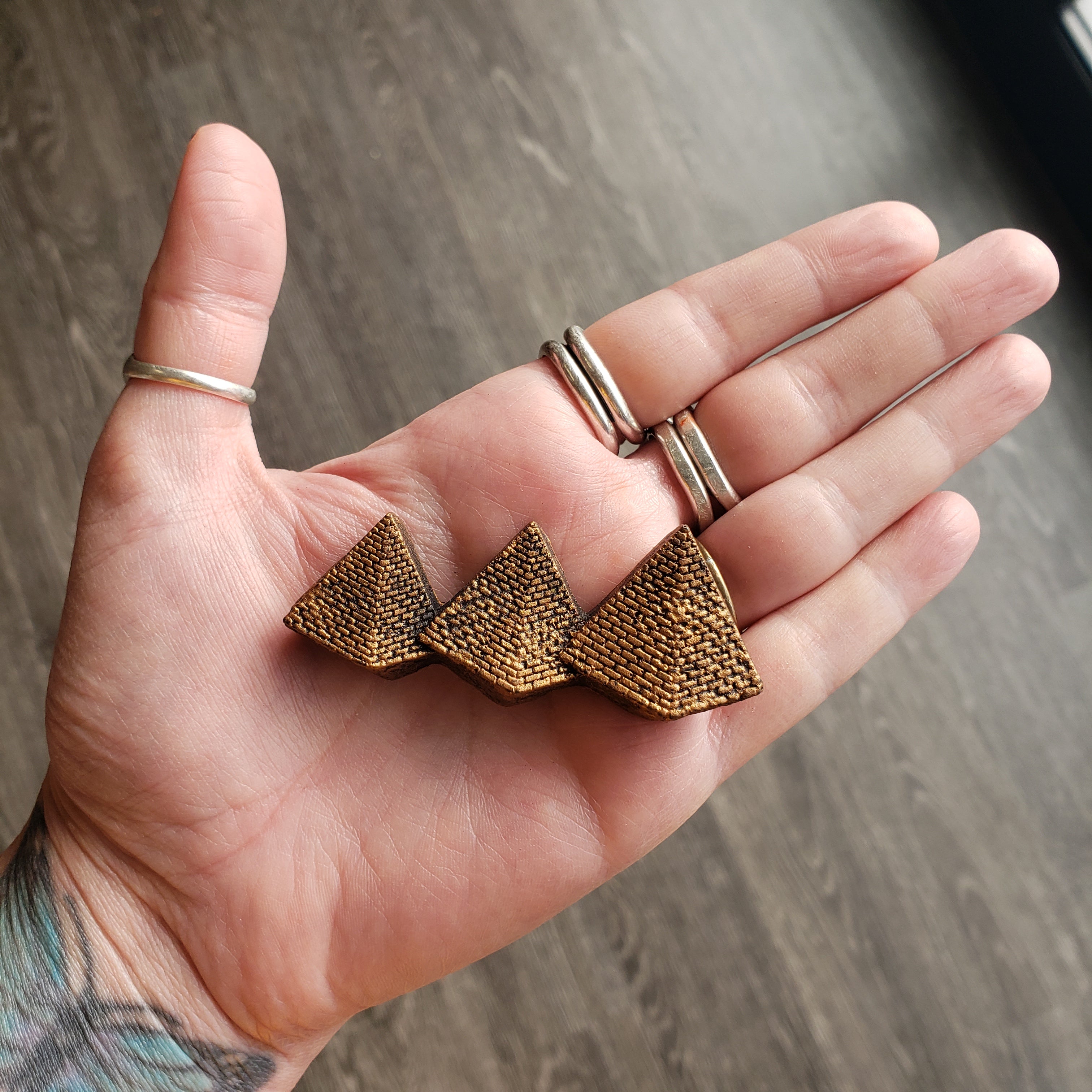 Hand holding a bronze geometric pendant against a wooden background