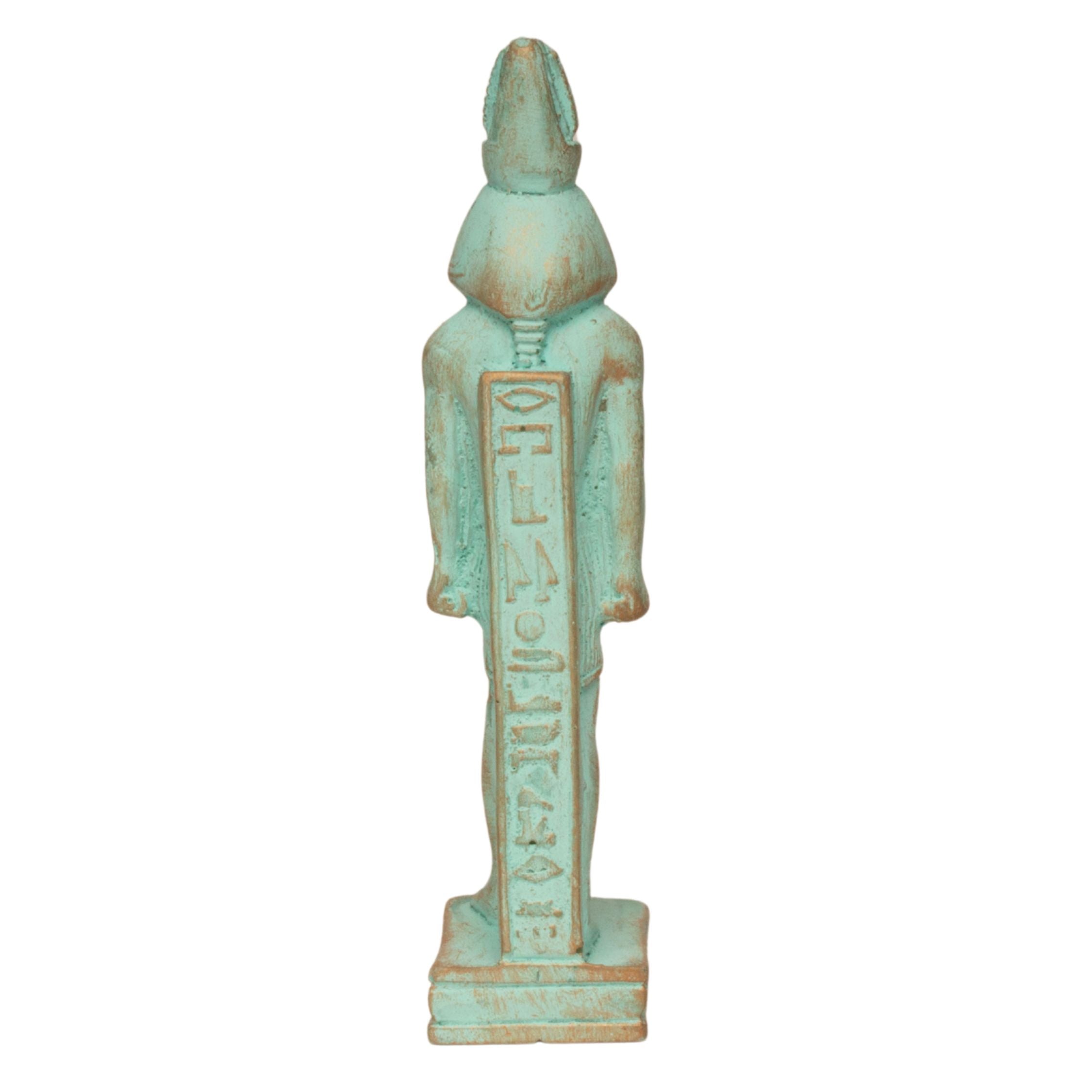 An Egyptian deity figurine with a distressed turquoise and brown finish, standing on a rectangular base and holding a vertical staff with hieroglyphs.