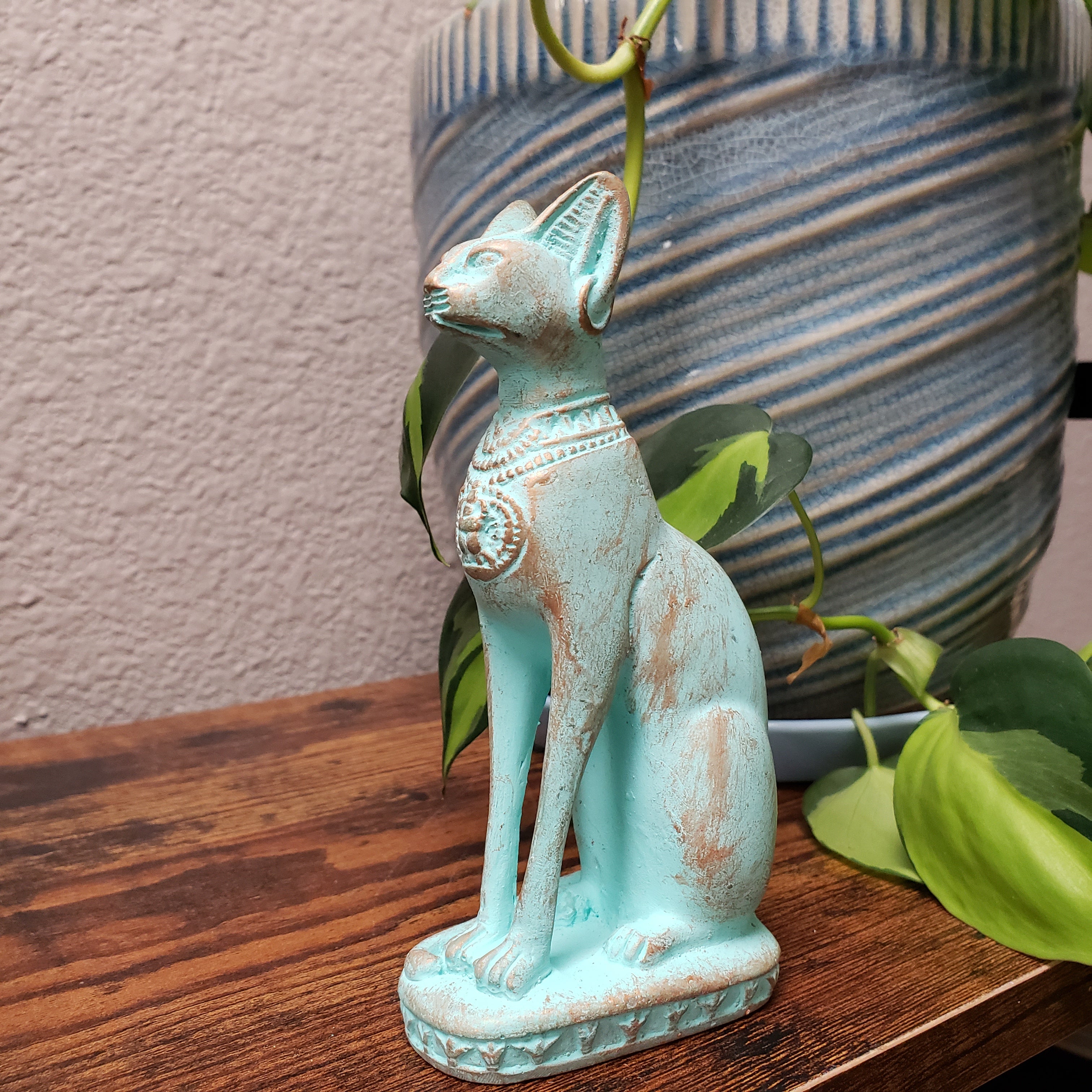 Decorative turquoise cat figurine with a plant on a wooden surface.