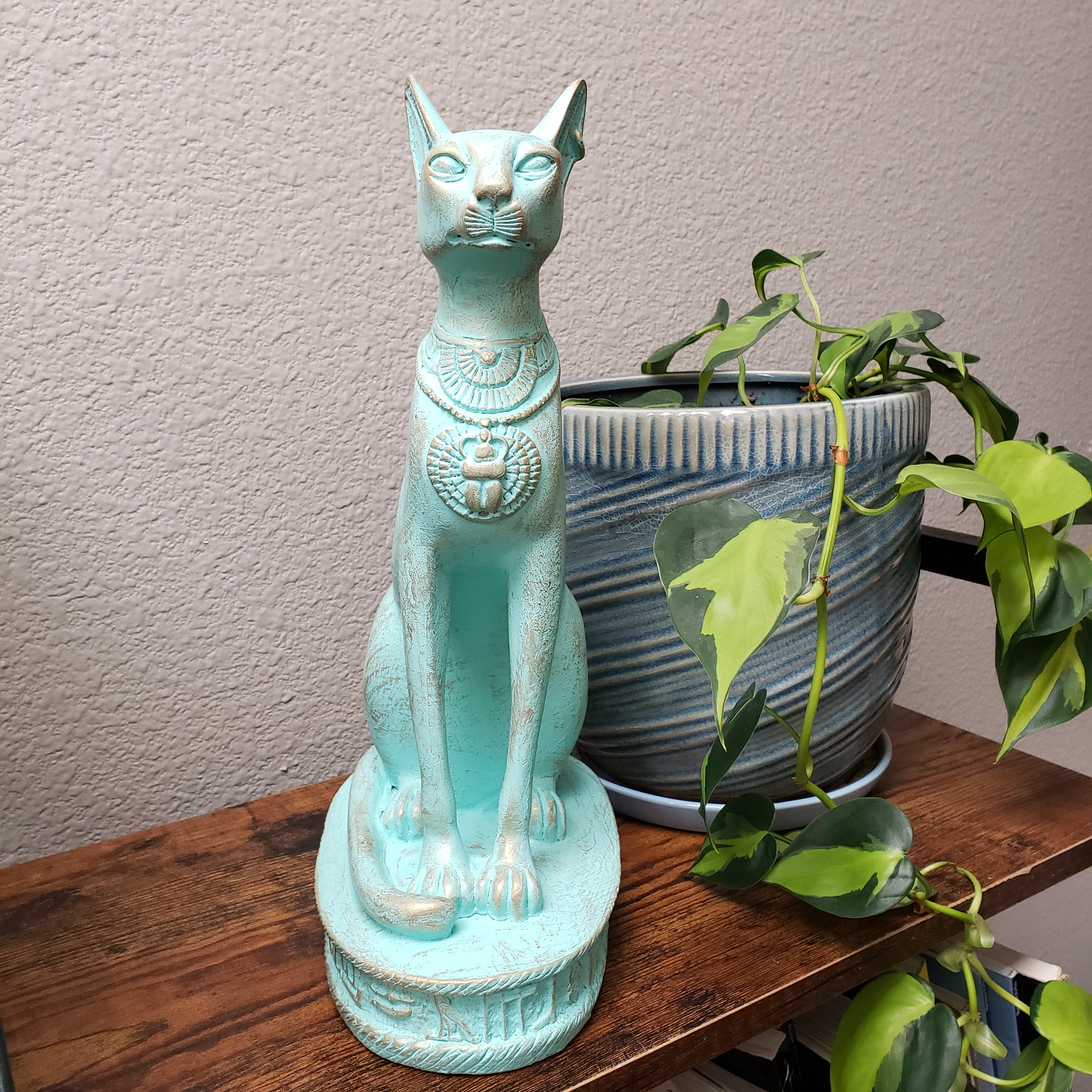Turquoise cat statue on a wooden surface with plants in the background