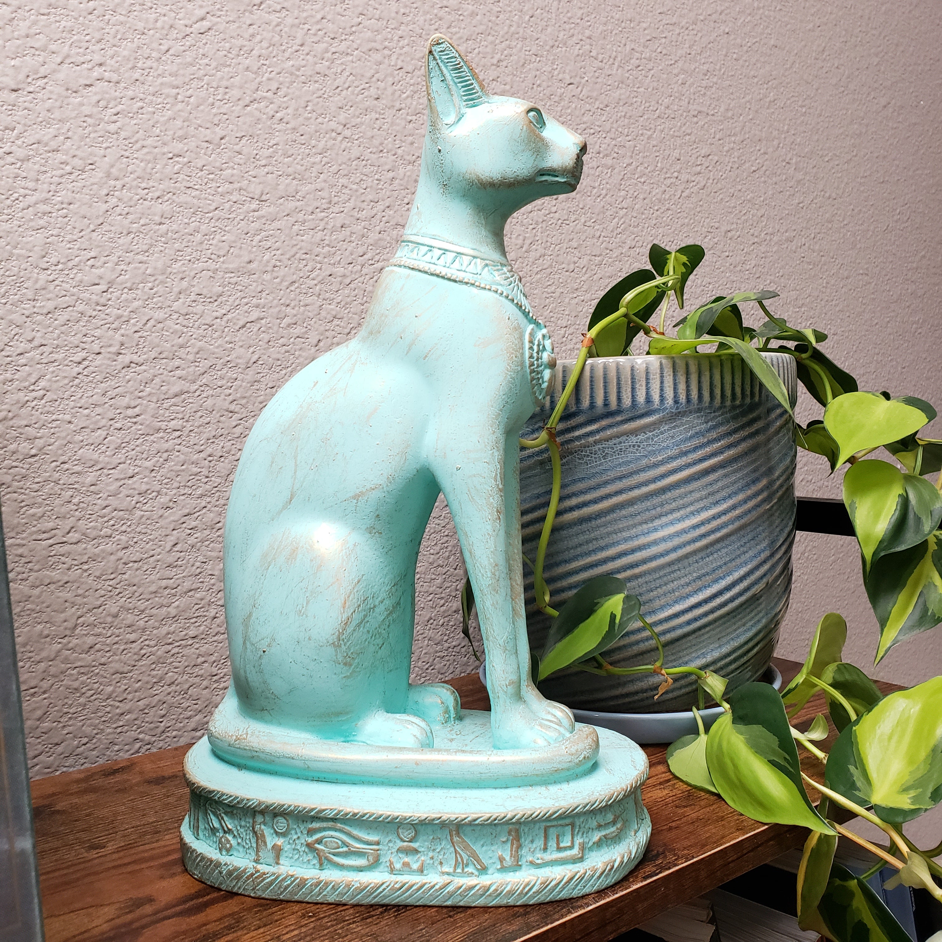 Turquoise cat-shaped planter with a plant on a wooden surface.