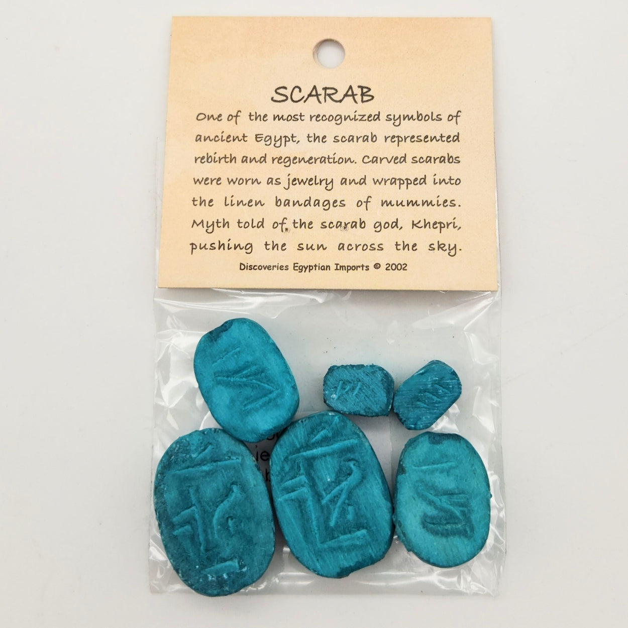 Packaged blue scarab stones with a descriptive label on a white background