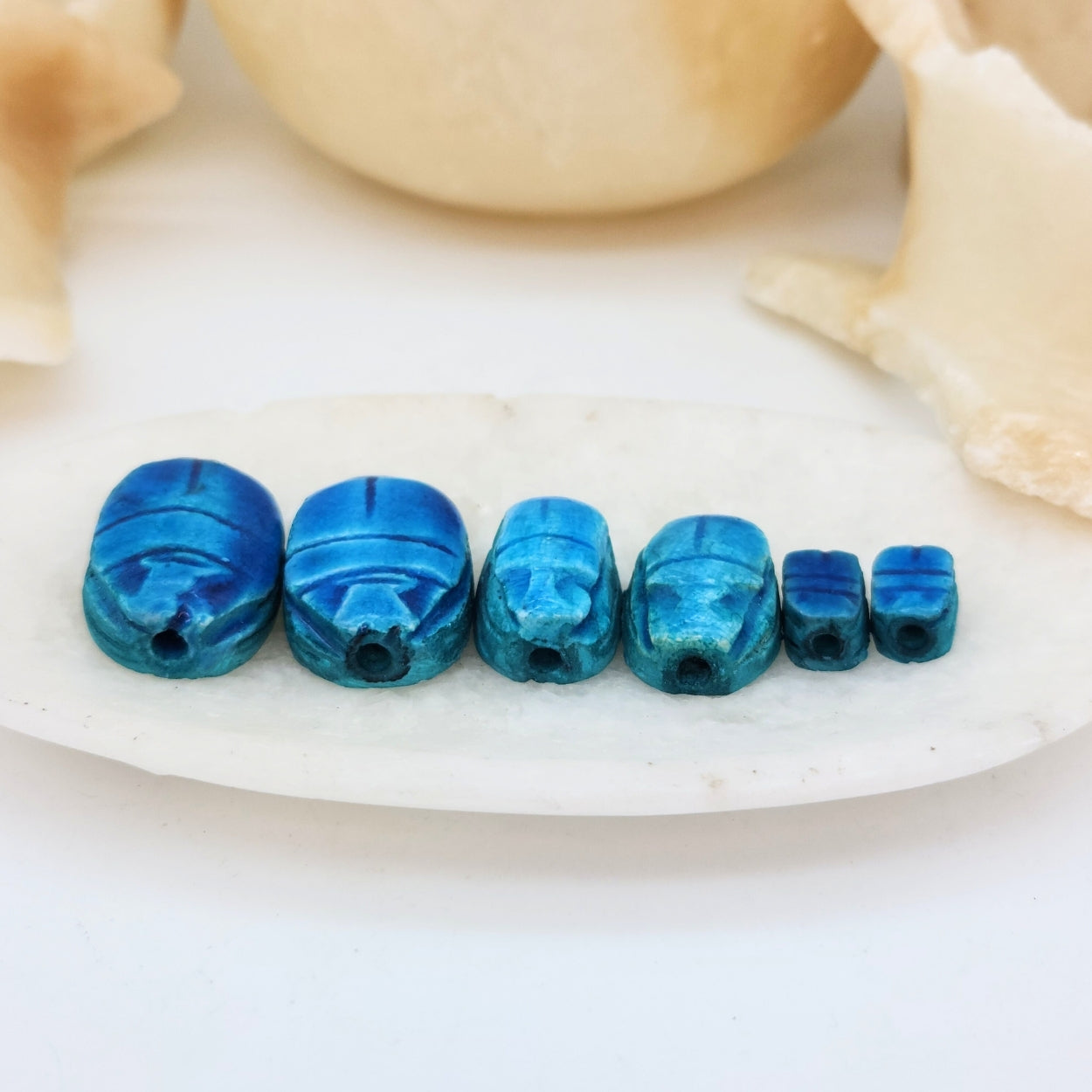 Blue scarab beads on a white shell with beige background