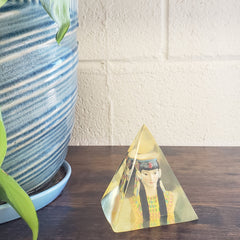 Decorative wall art with a woman's face on a wooden panel next to a textured white wall.